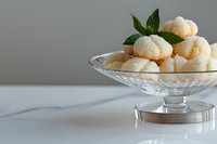 Delicate coconut macaroons served in elegant crystal dessert bowl on white surface, garnished with fresh mint leaves, minimalist food photography styling.