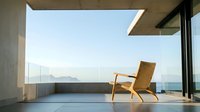 Wooden lounge chair on modern concrete terrace overlooking ocean and mountains, minimalist architecture with floor-to-ceiling windows, contemporary interior design.