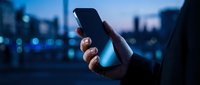 Close-up of hand holding smartphone with blank screen against blurred city skyline at night, representing mobile technology, connectivity, and urban digital communication.
