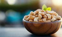 Fresh cashew nuts in wooden bowl with green leaf garnish on kitchen counter. Healthy snacking, cooking ingredients for recipes and nutritious food concepts.