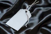 Blank white price tag with string attached on black silk fabric background, ready for branding, retail labeling, and product packaging design.