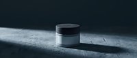 Luxury cosmetic jar with black cap on textured concrete surface with dramatic lighting and shadows for skincare product packaging design.