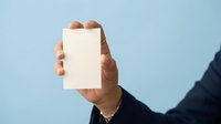 Male hand holding blank white card against blue background, suitable for business messaging, advertising mockups, and promotional designs.