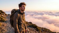 Male hiker with backpack standing on mountain peak above clouds at sunrise, adventure travel and outdoor exploration concept for hiking and trekking.