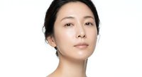 Young Asian woman with natural makeup and glowing skin looking confidently at camera against white background for beauty and skincare concepts.