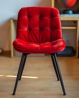 Modern red velvet dining chair with tufted upholstery and black metal legs on wooden floor, elegant furniture piece for contemporary interior design.