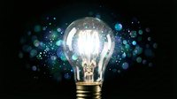 Glowing light bulb with bright illumination surrounded by blue bokeh particles on dark background representing innovation, creativity and bright ideas.