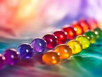 Colorful water gel beads arranged in rainbow spectrum on reflective surface with soft bokeh background. Macro photography shows transparent spheres with light refraction.