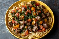 Tender beef meatballs with spaghetti pasta in yellow ceramic bowl, topped with fresh herbs, cherry tomatoes and colorful bell peppers on dark background.