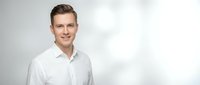 Confident young Caucasian businessman in white shirt smiling at camera against light gray background for corporate headshot and professional marketing.