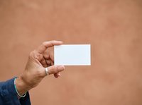 Close-up of male hand holding blank white business card against warm beige background. Suitable for corporate branding, business identity, and professional marketing materials.