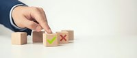 Businessman hand selecting wooden cube with green checkmark from row of blocks showing decision making and quality control process.