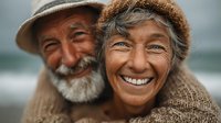 Happy elderly Asian couple embracing outdoors wearing warm knitted clothing and hats with genuine smiles showing love and companionship in golden light.