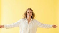 Young woman with shoulder-length blonde hair, Caucasian ethnicity, wearing white button-up shirt, arms outstretched in welcoming gesture against bright yellow background for lifestyle and wellness content.