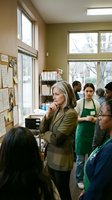 Mature Caucasian businesswoman in suit thoughtfully observing diverse team meeting in modern office workspace with natural lighting and bulletin board.
