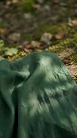Close-up of crumpled sage green linen fabric draped on natural ground with moss and stones, showcasing textile texture and earthy tones for design and lifestyle projects.