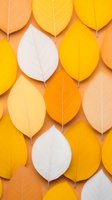 Colorful autumn leaves pattern in yellow, orange and white shades arranged in rows on peach background creating minimalist seasonal composition.