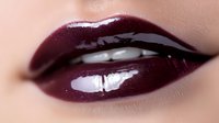 Close-up of glossy burgundy lips with dark wine lipstick and shimmer finish on fair skin for beauty and cosmetics advertising campaigns.