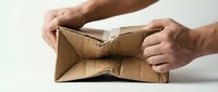 Hands of a man with medium skin tone holding an empty, worn cardboard box against white background, symbolizing poverty, financial hardship, or lack of resources.