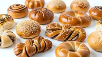 Assorted fresh baked bread rolls and pastries with seeds and glazed crusts arranged on white background for bakery menu design and food photography.