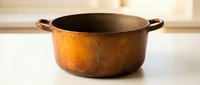 Vintage copper cooking pot with patina and handles on white surface, suitable for culinary, kitchen, and home decor projects.