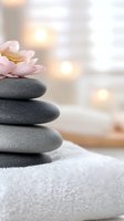 Stacked spa stones with pink lotus flower on white towel against soft bokeh background. Zen wellness concept for massage therapy and meditation practices.