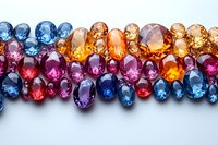 Colorful sapphire and precious gemstones arranged in rows showing natural variety of colors from blue to orange, pink and purple on white background for jewelry design.