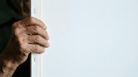 Mature man with weathered hands gripping white door frame, showing age spots and wrinkles. Suitable for healthcare, aging, vulnerability, and lifestyle editorial content.