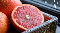 Fresh ripe grapefruit cut in half showing juicy pink flesh with water drops, whole citrus fruits in rustic wooden box, moody natural lighting.