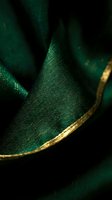 Closeup of luxurious emerald green fabric with gold trim detail, showcasing rich textile texture and elegant material for fashion, design, and luxury product applications.