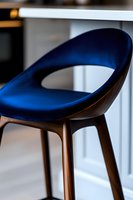 Modern bar stool with curved blue velvet upholstery and wooden base, showcasing contemporary furniture design in minimalist interior setting.
