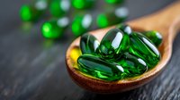 Green transparent vitamin E capsules in wooden spoon on dark background. Natural dietary supplements and alternative medicine concept for healthy lifestyle.