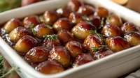 Glazed pearl onions with fresh herbs in white ceramic baking dish, perfect holiday side dish for Thanksgiving and Christmas dinner celebrations.