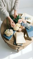 Woman arranging pastel roses and hydrangeas on wooden table with vintage books for wedding planning, floral design, or romantic home decor styling.