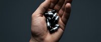 Adult male hand holding multiple black and white medication capsules against neutral background for healthcare and pharmaceutical concepts.