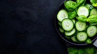 Fresh sliced cucumber with basil leaves in black bowl on dark background with copy space. Clean eating and healthy food concept.