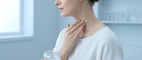 Young Caucasian woman touching her neck while holding a cream jar in a bright clinic, skincare and thyroid health concept.