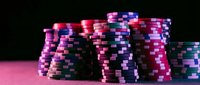 Colorful casino poker chips stacked on pink gaming table against dark background for gambling entertainment and betting games.