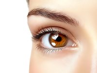 Close-up of woman's amber brown eye with long eyelashes and natural eyebrow showing detailed iris patterns and healthy skin texture for beauty concepts.
