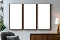 Three vertical wooden frame mockups on gray wall above wooden sideboard in modern living room interior with cozy armchair and table lamp.