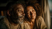 Happy African American senior man with gray beard laughing with young woman in warm indoor setting showing intergenerational family bond and joy.