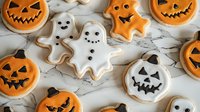 Festive Halloween sugar cookies decorated with royal icing featuring spooky ghosts and grinning jack o'lantern pumpkins on marble surface, seasonal holiday treats.