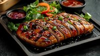 Grilled chicken breast with teriyaki glaze and sesame seeds sliced on black stone plate, served with fresh vegetables and dipping sauces for restaurant menu.