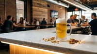 Fresh beer mug with foam on bar counter in modern brewery restaurant with blurred people dining in background for hospitality industry marketing.