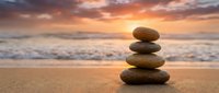 Balanced stone stack on beach at sunset with golden sky and ocean waves creating peaceful zen meditation scene for wellness and mindfulness concepts.