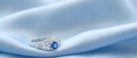 Elegant diamond engagement ring with blue sapphire center stone on white silk fabric, luxury jewelry for weddings and special occasions.