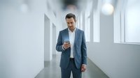 Mature male professional with dark hair and facial hair wearing blue business suit walking through modern white corridor, checking wristwatch, suitable for corporate, business, and professional lifestyle content.