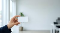 Businessman holding blank white business card in modern office environment with natural light and blurred background for branding and corporate identity.