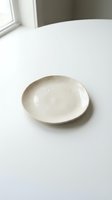 Empty ceramic plate on white table near window with natural light for minimalist dining and kitchen design concepts.