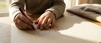 Young woman artist sketching creative drawings on paper at wooden desk in warm natural light for artistic hobby and creative expression projects.